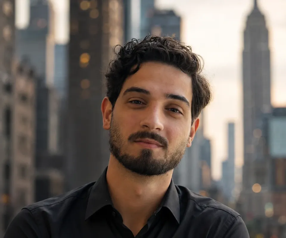 Retrato do Gustavo, de camisa preta, com a cidade desfocada ao fundo